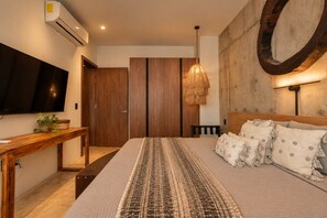 A bedroom with a bed, a TV, a wooden desk, and a wall-mounted mirror. - Tulum 2BR Swim-Out Retreat | 3 Smart TVs & Rooftop Pool (Tulum)