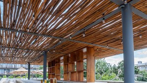Un espace bar extérieur doté d’un plafond en lambris de bois, d’un comptoir en béton et de chaises en osier.