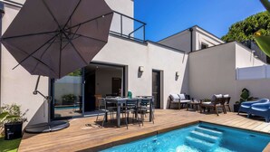 Una piscina con muelle de madera, muebles de exterior y un gran paraguas.