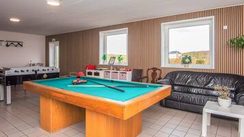 Una mesa de billar en una habitación con un sofá y una mesa de fútbolín.