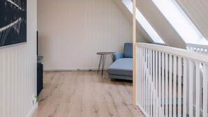 A loft bedroom with a sloped ceiling, a small table, a sofa, and a view of the outside. - 4 Star Holiday Home in Hojer (Højer)