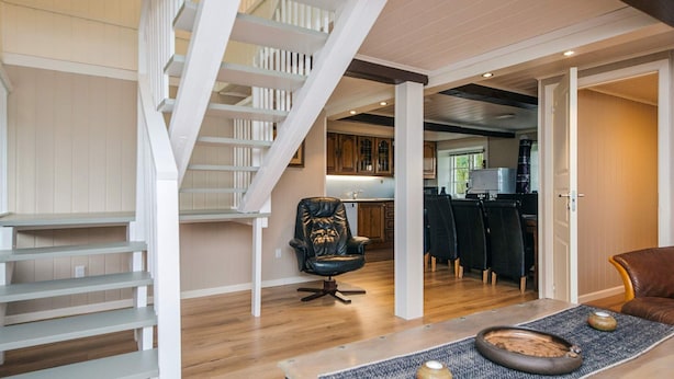 A modern interior with a staircase, a dining area with chairs, and a kitchen in the background. - 4 Star Holiday Home in Hojer (Højer)