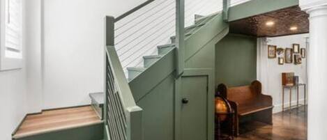 Una escalera con barandilla verde que lleva a una plataforma con un banco y una pared adornada con cuadros.