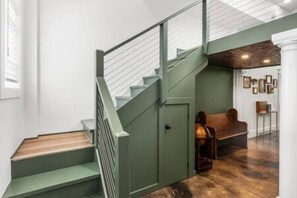 Eine Treppe mit grüner Geländer, die zu einer Empore mit einer Bank und einer Wand mit gerahmten Bildern führt.