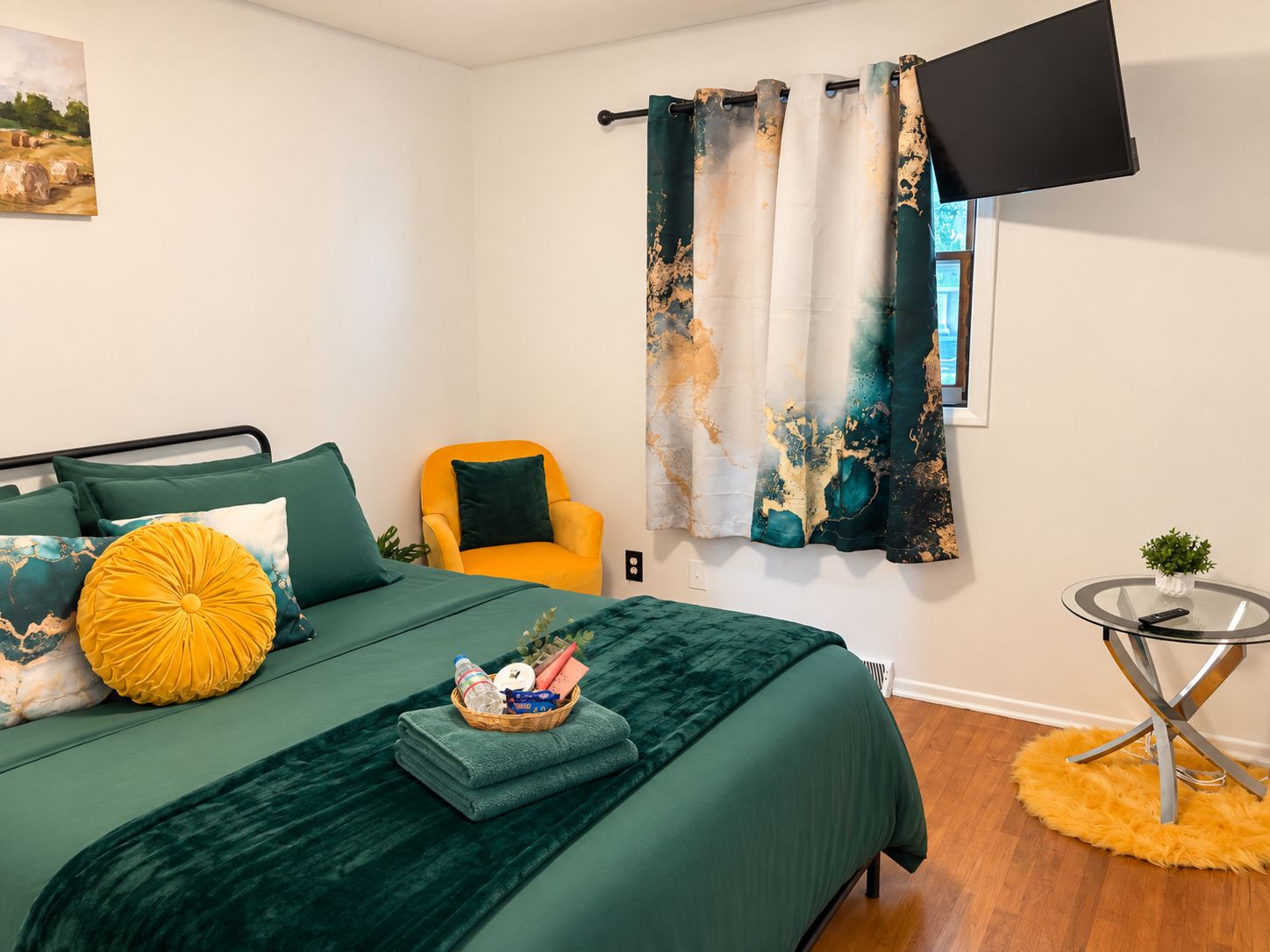 Quarto com cama, cadeira, televisão e uma pequena mesa com uma planta.