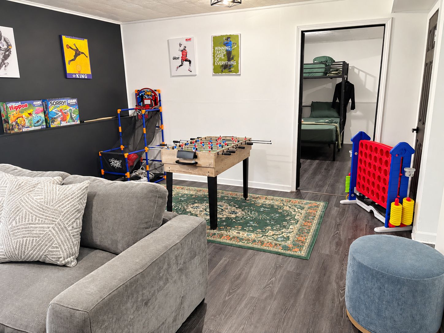 A living room with a grey sofa, a foosball table, and a small ottoman.