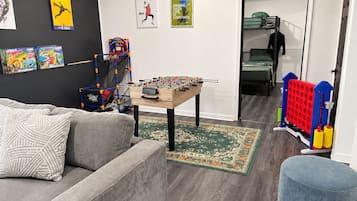 A living room with a grey sofa, a foosball table, and a small ottoman.