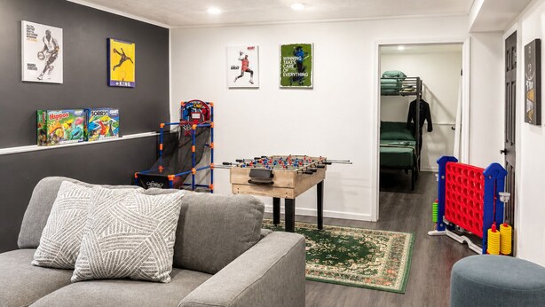 Ein Wohnzimmer mit grauem Sofa, einem Kicker und einem Basketballkorb.