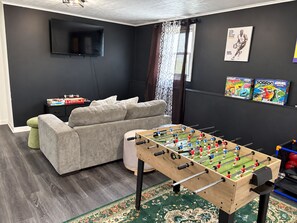 A living room with a foosball table, a sofa, a television, and a window with curtains.