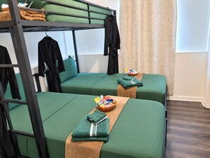 A bunk bed room with two green beds, a wooden ladder, and a small table with toiletries.