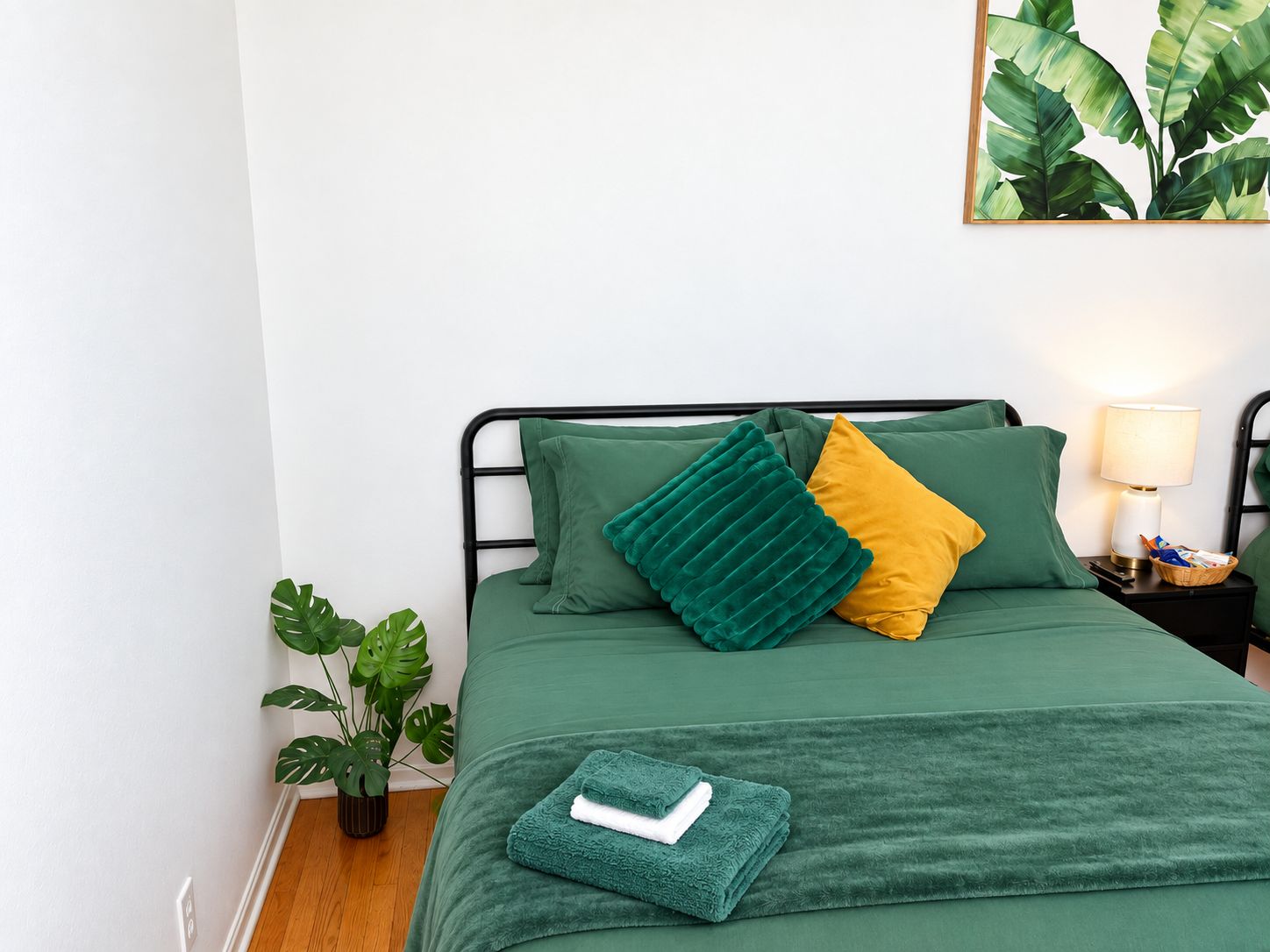 A neatly made bed with a green bedspread, two pillows, a bedside lamp, and a small plant beside the bed.