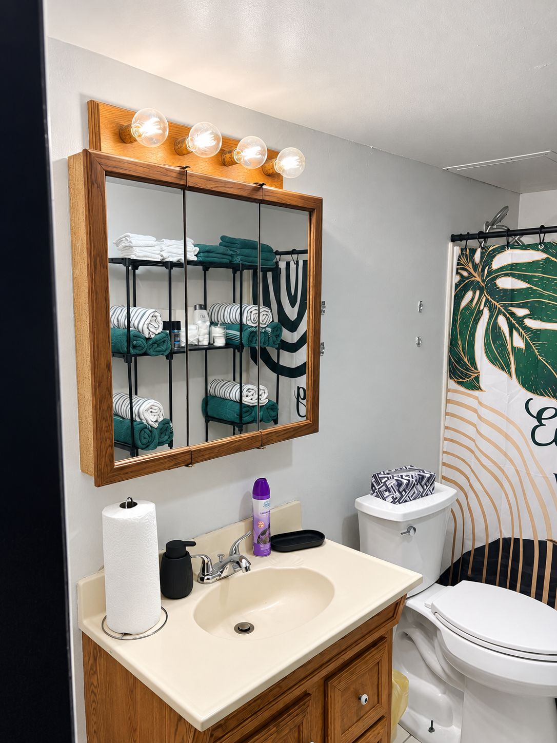 Ein Badezimmer mit einem Holzwaschtisch, einem Spiegel, einer Toilette und einem Duschvorhang mit Blattmuster.