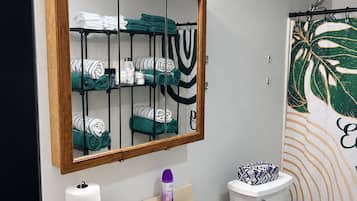 Ein Badezimmer mit einem Holzwaschtisch, einem Spiegel, einer Toilette und einem Duschvorhang mit Blattmuster.