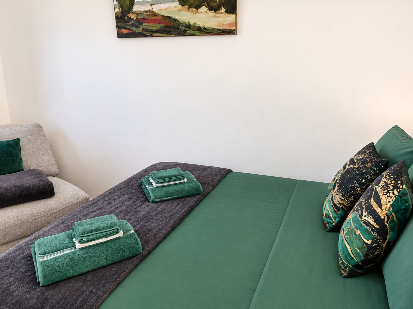 A hotel room with a bed, a sofa, and a painting on the wall.