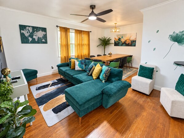 A modern living room with a sectional sofa, a dining table, and a ceiling fan.