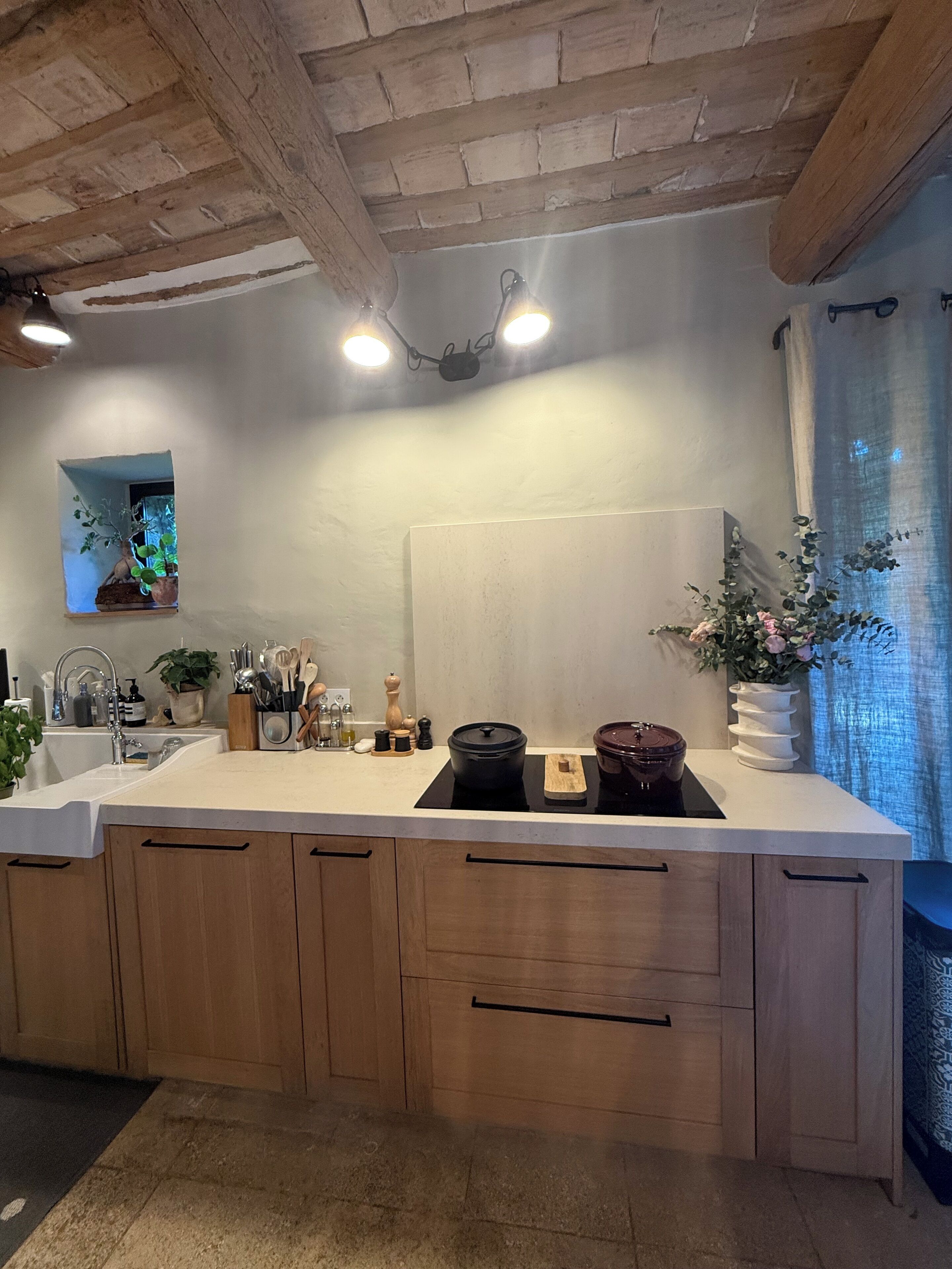 Une cuisine avec un plan de travail blanc, des armoires en bois, une plaque de cuisson à induction noire et un luminaire suspendu.
