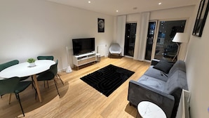 Una sala de estar moderna con comedor, televisor de pantalla plana, sofá gris y alfombra negra.