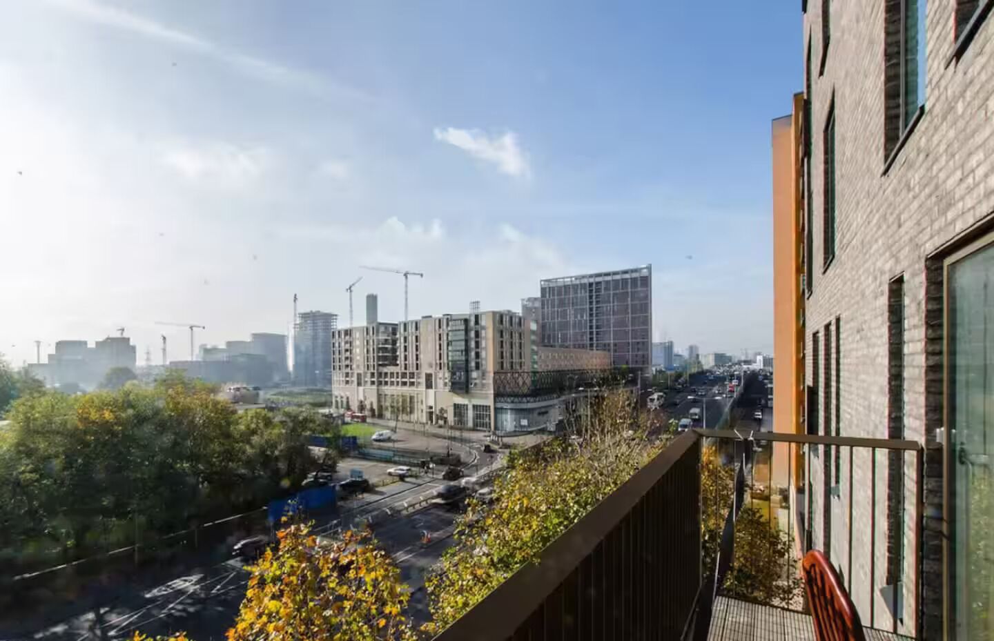 A modern building with a rooftop garden, surrounded by other high-rise structures and a busy street below.