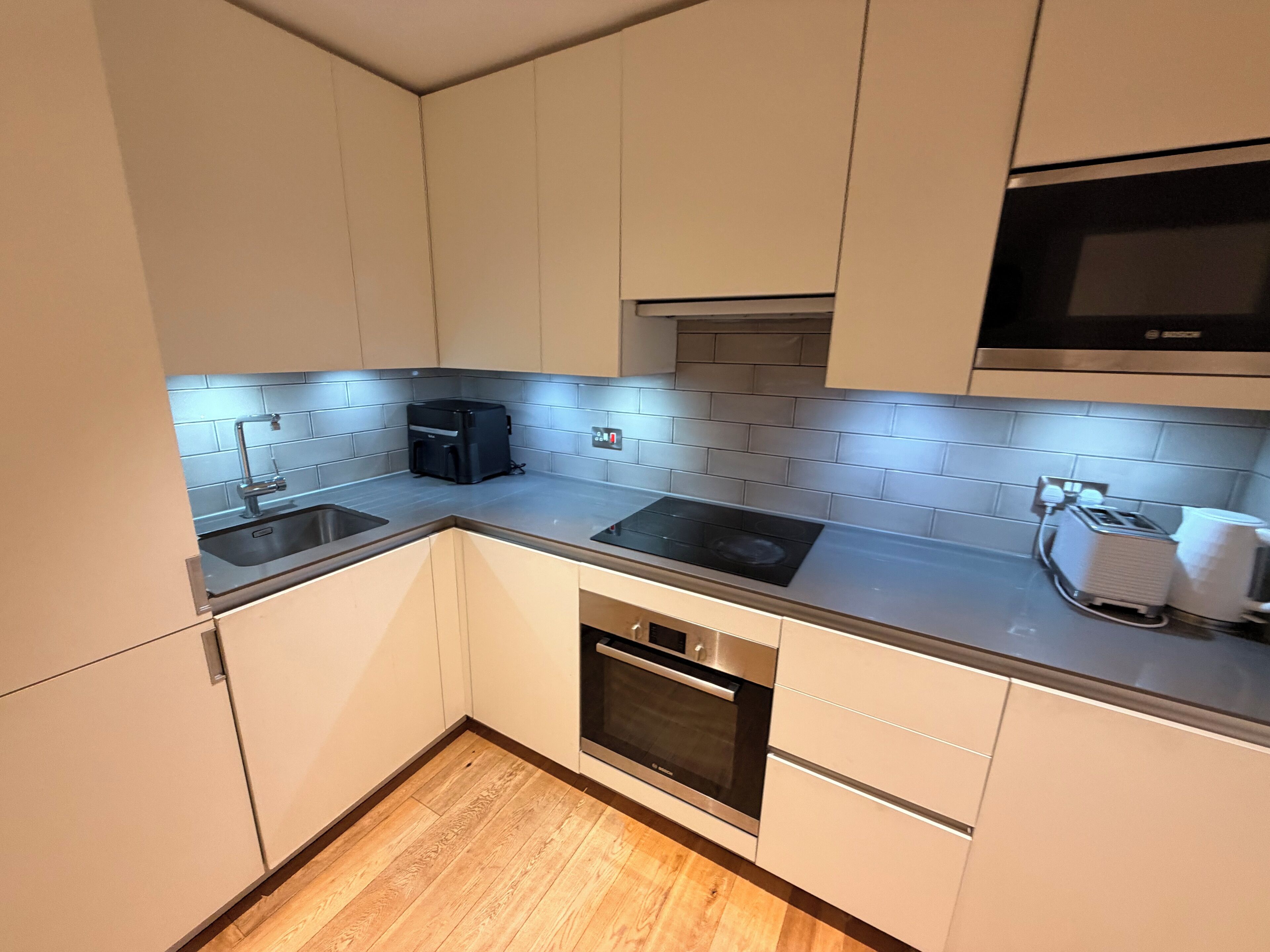 Eine kleine Küche mit weißen Schränken, einer Edelstahl-Spüle, einem Backofen und einer Mikrowelle.