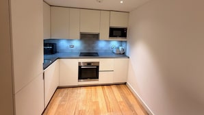 Una cocina compacta con gabinetes blancos, un microondas, un tostador y un horno empotrado.