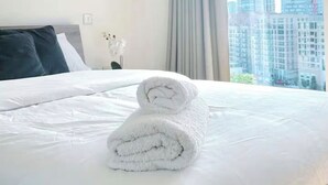 Habitación de hotel con una cama bien hecha, una ventana con cortinas y vistas a edificios altos.