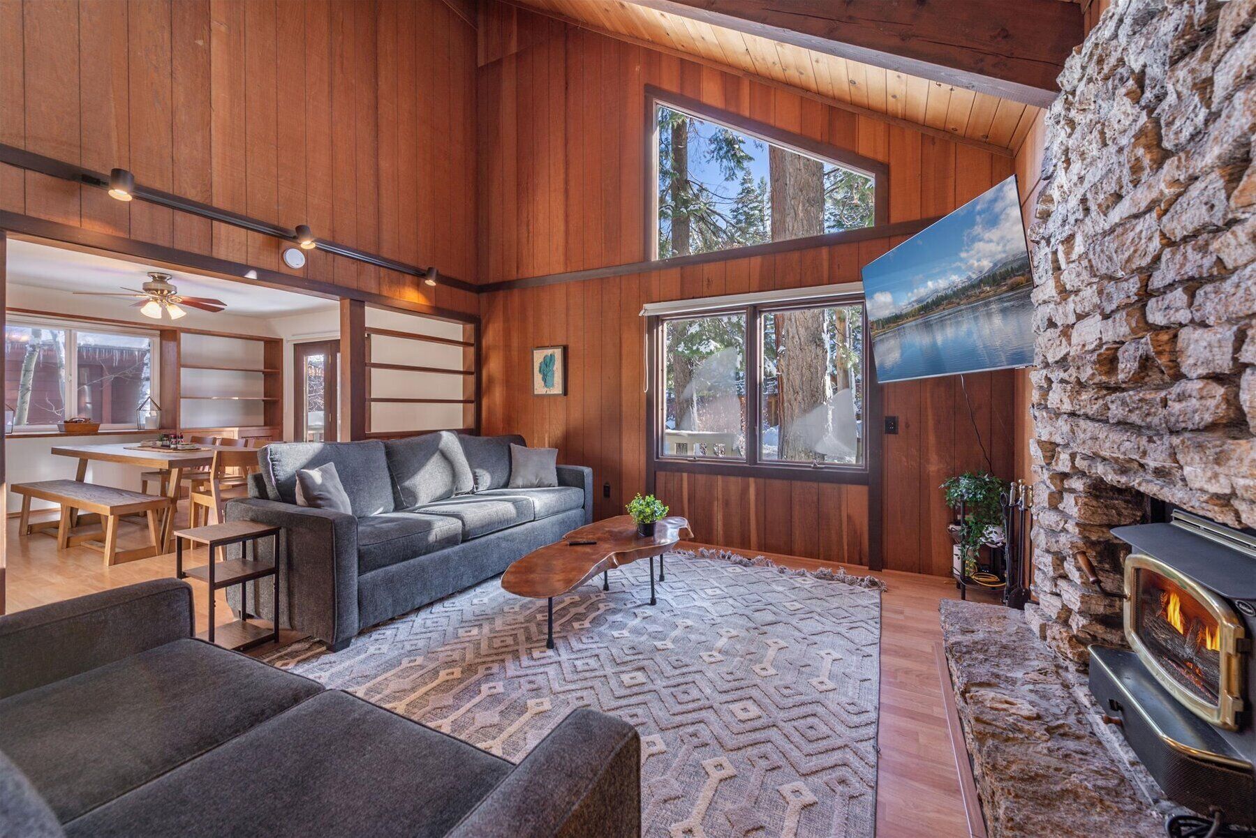 A cozy cabin interior with a fireplace, wooden walls, a sofa, and a dining area.