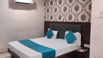 Una cama bien hecha con un cubrecolcha azul, una mesita de noche con un teléfono y un papel tapiz estampado.