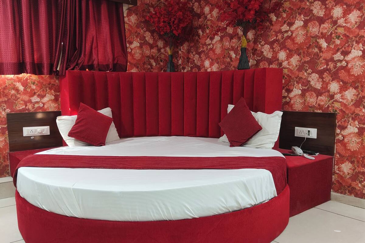 A modern bedroom with a curved bed, red bedding, a floral wallpaper, and a built-in air conditioning unit.
