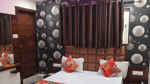 A neatly arranged bedroom with a large bed, a wooden headboard, a ceiling fan, and a wall with a unique spherical pattern. - HOTEL LOTUS GOLD (Vadodara)