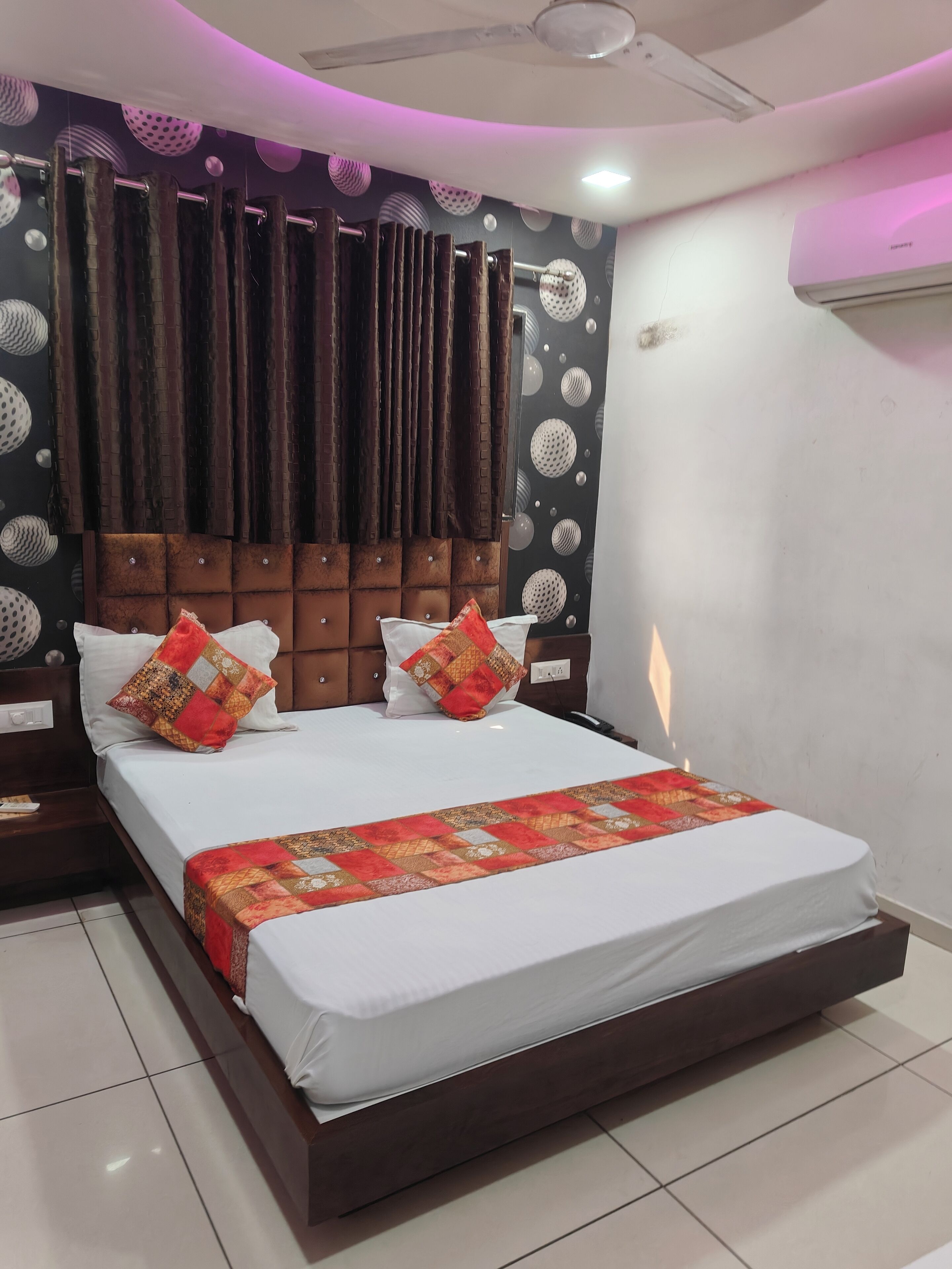 A modern bedroom with a large bed, dark wooden headboard, and patterned wall decor.