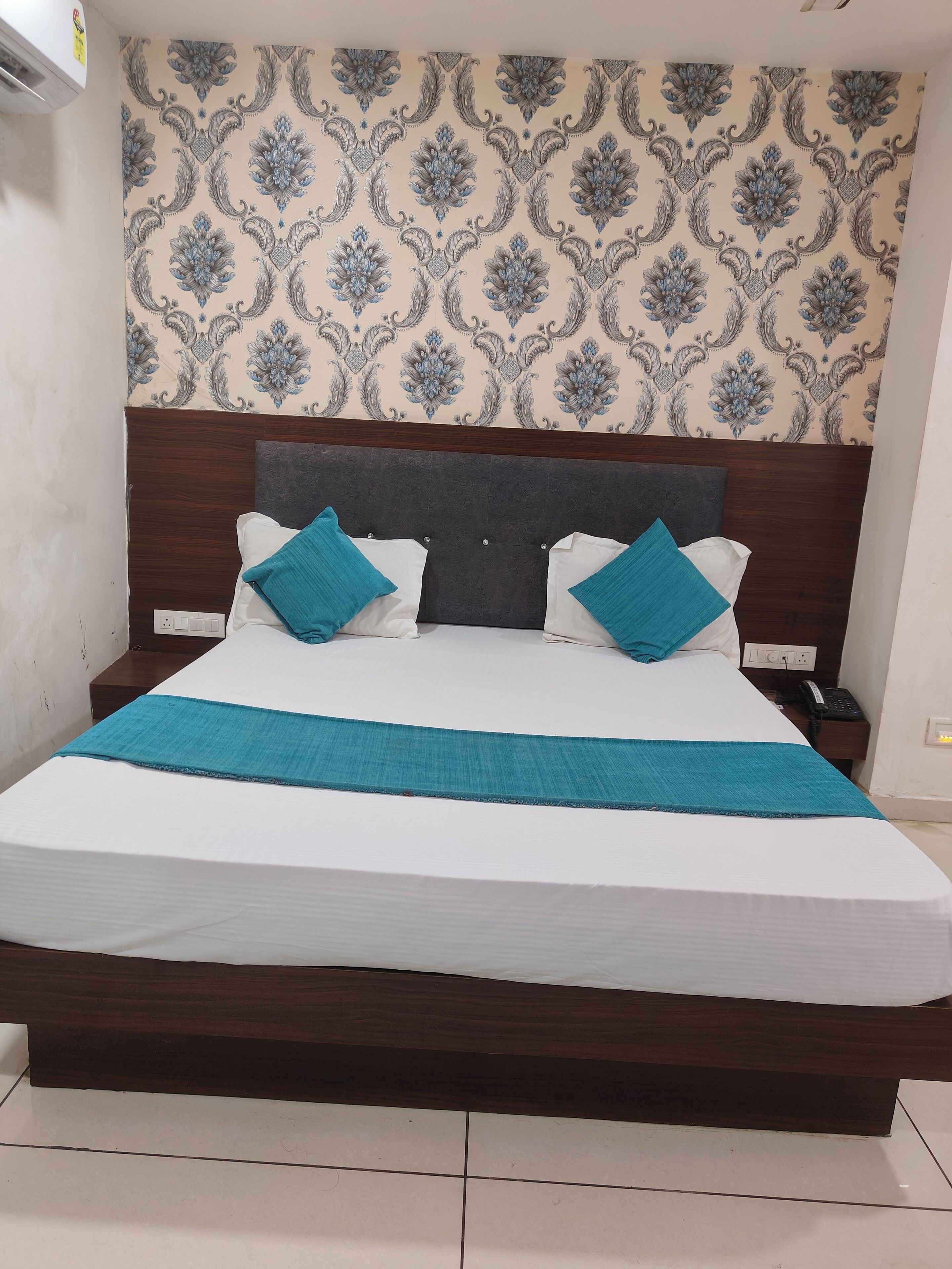 Un grand lit avec une tête de lit en bois, une literie blanche et deux coussins décoratifs de couleur turquoise.