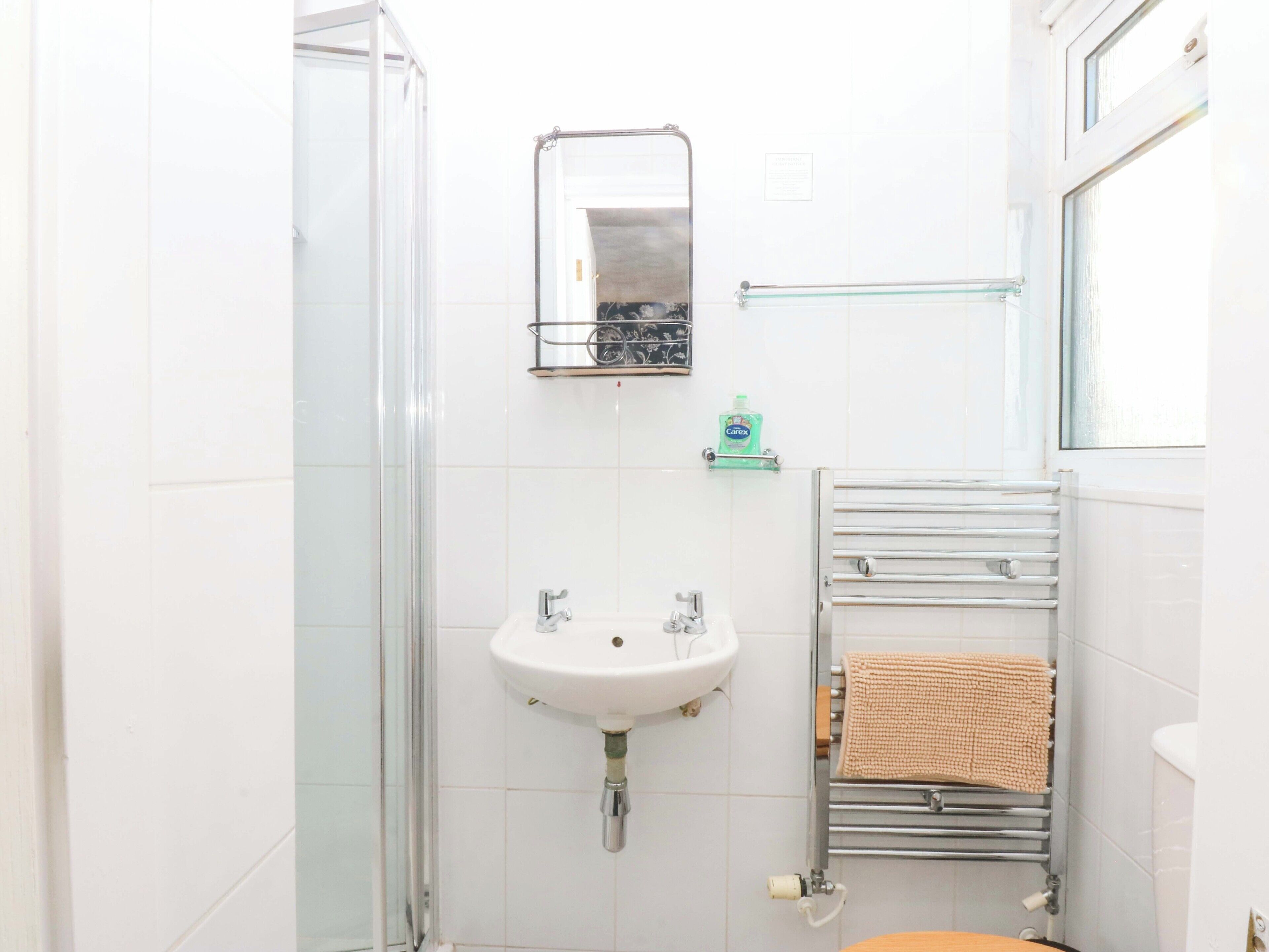 A bathroom with a glass shower enclosure, a white sink with a mirror above it, and a towel rack with a beige towel.