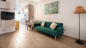 A modern living room with a green sofa, a flat-screen TV, a dining area with a table and chairs, and a kitchen in the background. - 3-minute walk from Metro Line B, P. Bologna, Tiburtina Station (Airport Link), 2 bedrooms, 2 bathrooms, A/C, Wi-Fi (Roma)