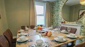 A dining room with a long wooden table set for a meal, surrounded by upholstered chairs. - Curzon Heights (Llandudno)