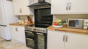 A modern kitchen with a stove, oven, microwave, and white cabinets. - Curzon Heights (Llandudno)