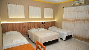 A hotel room with three single beds, a wooden headboard, a small table, and a curtain with a floral pattern. - Hotel Vitória Régia (Engenheiro Beltrão)