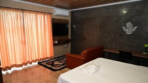 A hotel room with a bed, a desk, a chair, a television, and a wall-mounted air conditioner. - Hotel Vitória Régia (Engenheiro Beltrão)
