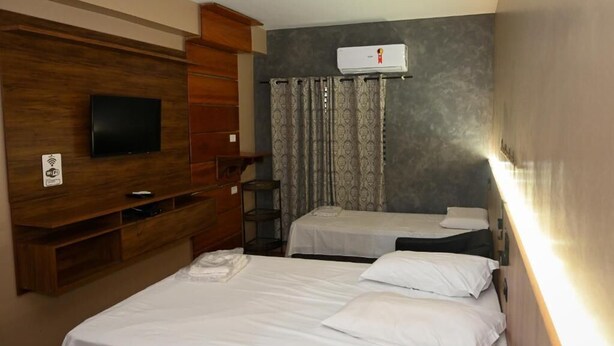 A hotel room with two beds, a TV, a wardrobe, and an air conditioning unit. - Hotel Vit ória Régia (Engenheiro Beltrão)