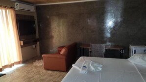 A hotel room with a bed, a small table, a chair, an air conditioning unit, and a television. - Hotel Vitória Régia (Engenheiro Beltrão)