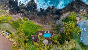 Vista aérea de una propiedad costera con piscina, abundante vegetación y un litoral rocoso.