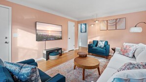 Ein Wohnzimmer mit einem großen Flachbildfernseher, einem blauen Sessel, einem weißen Sofa und einem Holztisch.