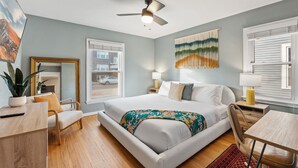 Ein Schlafzimmer mit Bett, Nachttischen, Schreibtisch, Stuhl, Deckenventilator und Fenster.