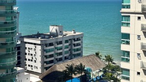 A high-rise hotel with a view of the sea, a pool area, and a thatched-roof structure. - Premium Ocean View Penthouse in Meia Praia - 12th floor, high standard, one block from the beach. (Itapema)