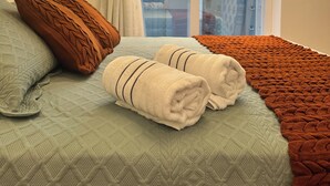 A neatly made bed with a quilted cover, two rolled towels, and a brown knitted blanket. - Premium Ocean View Penthouse in Meia Praia - 12th floor, high standard, one block from the beach. (Itapema)