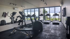 Ein Fitnessstudio mit unterschiedlichen Trainingsgeräten, großen Fenstern und Meerblick.