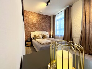 Une chambre avec un mur en briques, un lit blanc et une table de chevet.