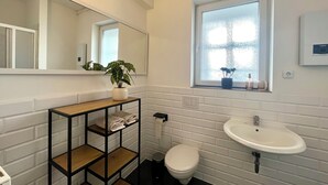 Une salle de bain moderne avec un mur recouvert de carreaux blancs, un meuble-lavabo en bois avec un miroir, un lavabo blanc et une fenêtre offrant une belle vue.