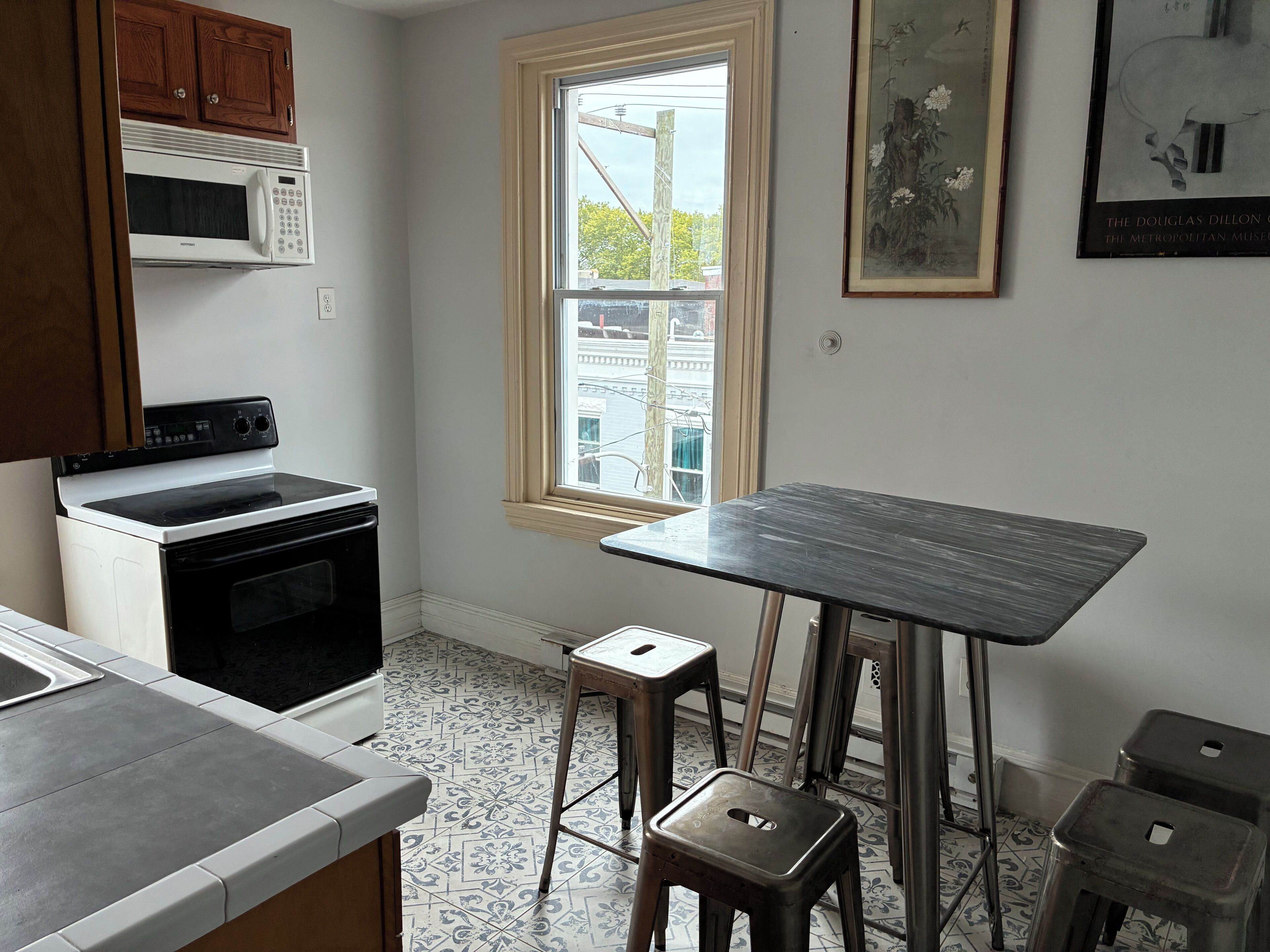 A kitchen with a microwave, stove, and sink. There is a window with a view of buildings outside.