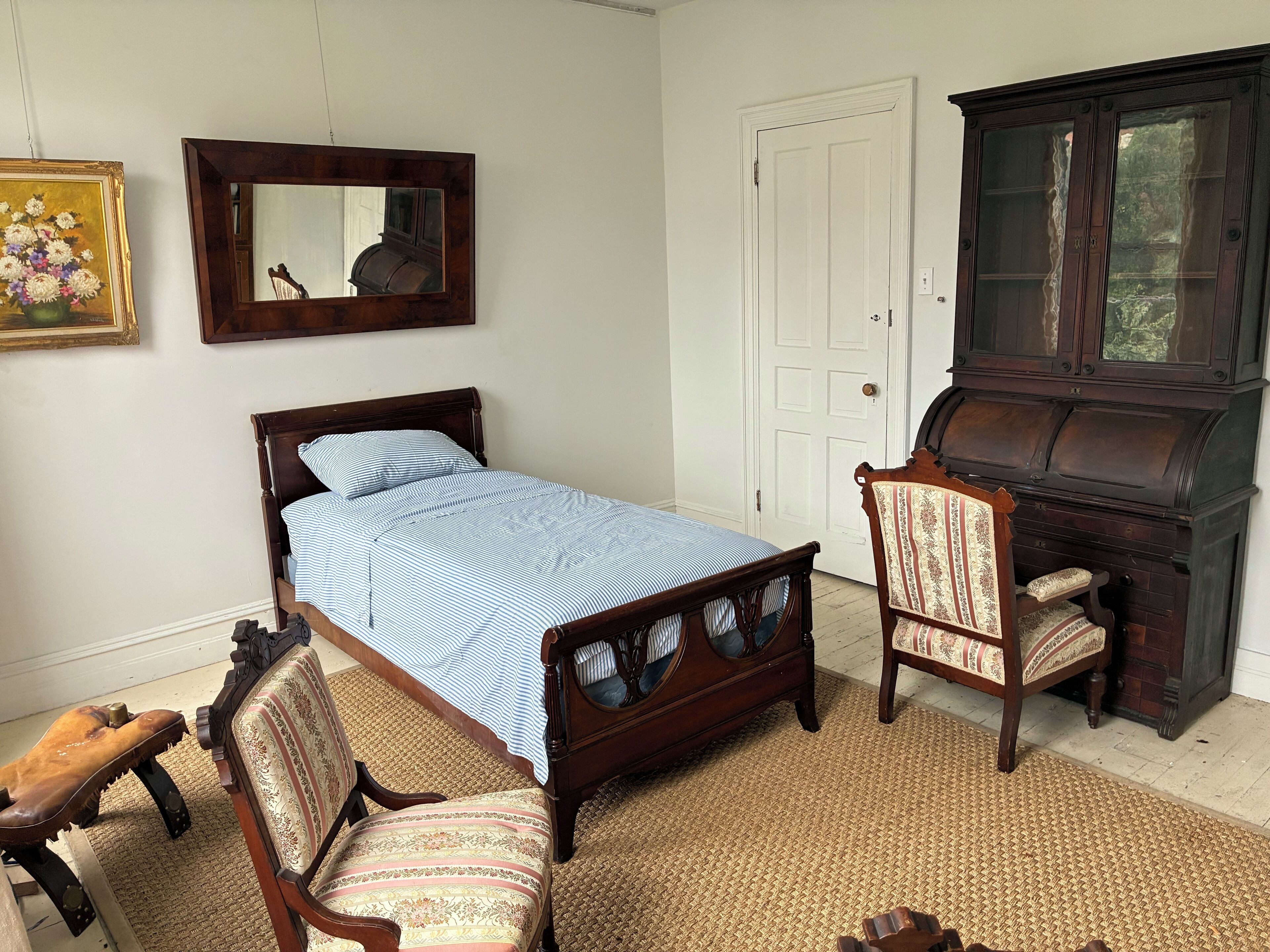 Un dormitorio con cama, una silla, cómoda y espejo.
