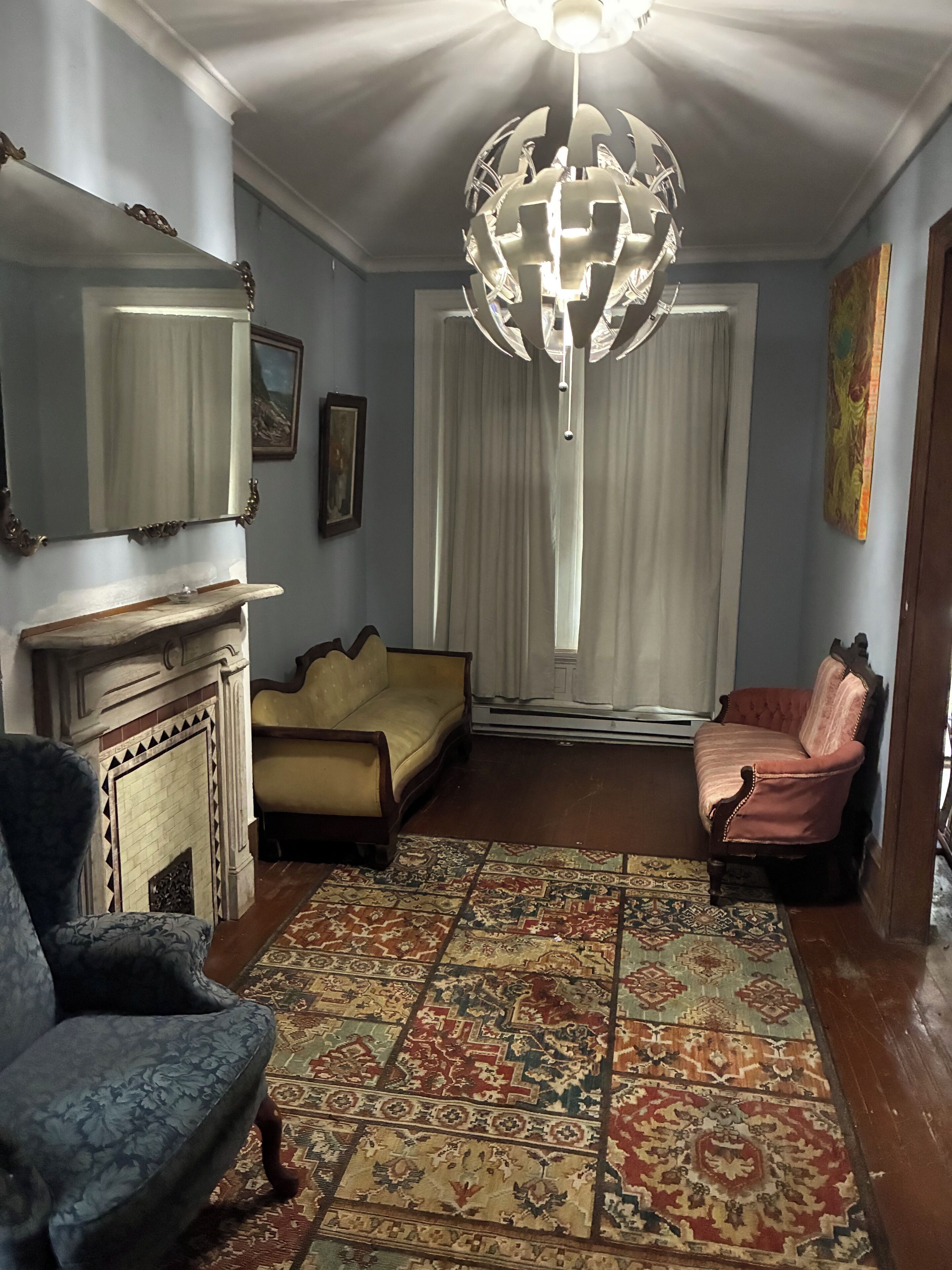 A room with a fireplace, two sofas, a patterned rug, a chandelier, and a large mirror.